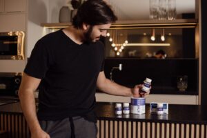 Adult man in modern kitchen examining various health supplements for fitness and wellness.