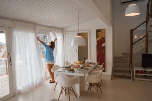 Bright dining room with modern decor and a person opening curtains, creating a warm and inviting atmosphere.