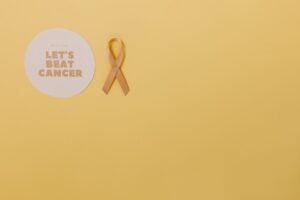 Minimalist design featuring a gold cancer awareness ribbon on yellow background.
