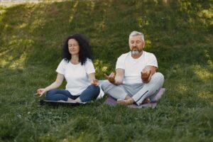A senior couple meditates together outdoors on yoga mats, promoting a healthy lifestyle.