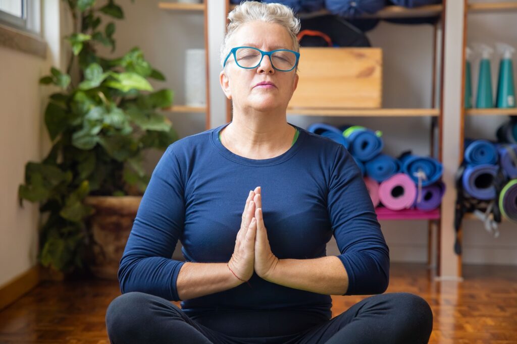 A senior woman practices yoga indoors, focusing on relaxation and mindfulness with closed eyes.