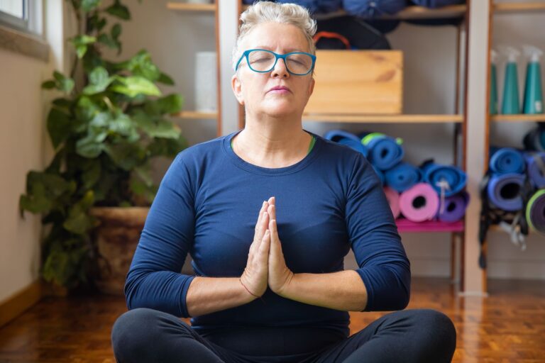 A senior woman practices yoga indoors, focusing on relaxation and mindfulness with closed eyes.