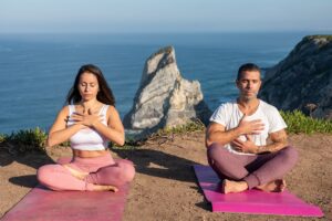 Man and woman practicing meditation on yoga mats by the ocean in Portugal.