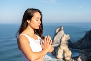 A woman meditates peacefully by the ocean in Portugal, embracing wellness.