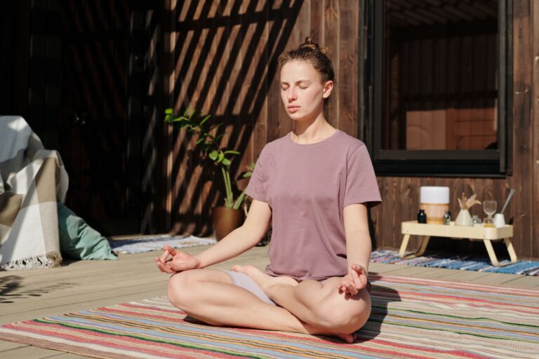 Woman practicing meditation in lotus pose on a sunny outdoor deck.